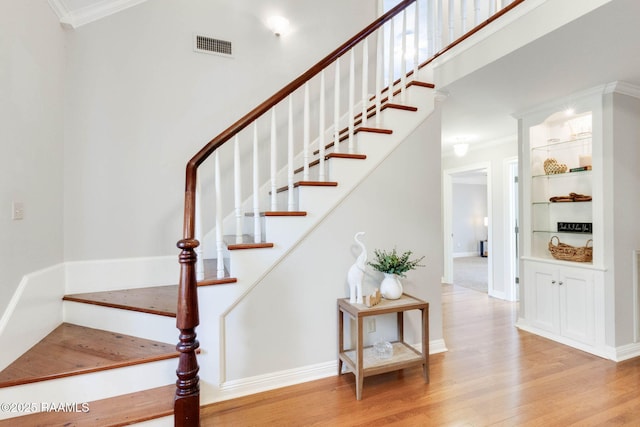 stairway with visible vents, ornamental molding, a high ceiling, and wood finished floors