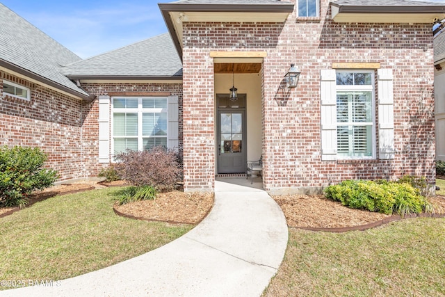 entrance to property featuring a yard, brick siding, and roof with shingles