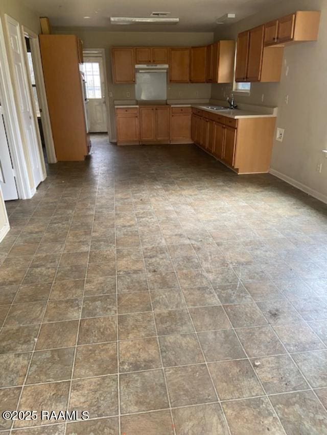 kitchen with brown cabinets, light countertops, a sink, under cabinet range hood, and baseboards