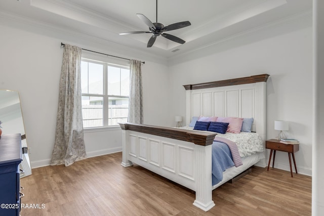 bedroom with baseboards, visible vents, light wood-style flooring, ornamental molding, and a raised ceiling