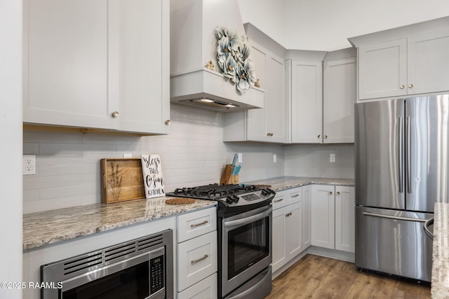 kitchen with light wood-style floors, stainless steel appliances, light stone countertops, and backsplash