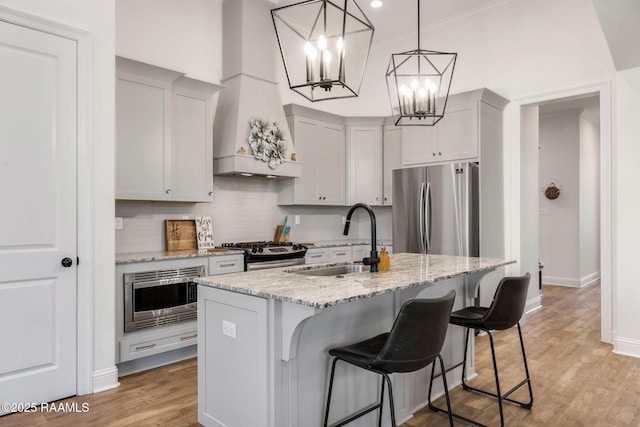 kitchen with a kitchen bar, a sink, backsplash, stainless steel appliances, and light wood-style floors