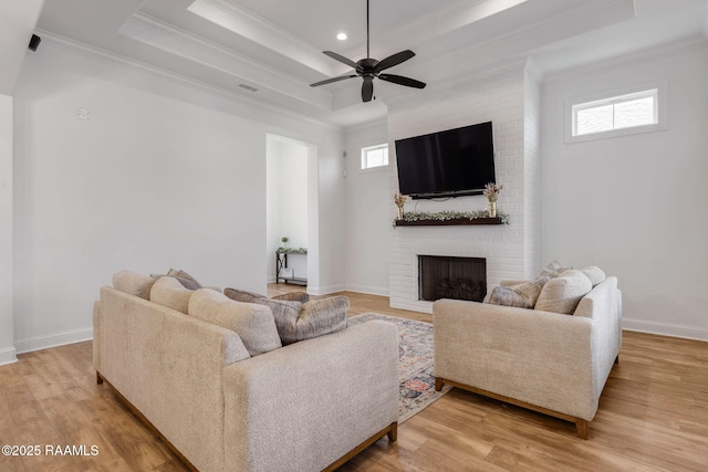 living room featuring a raised ceiling, a healthy amount of sunlight, a fireplace, and light wood finished floors