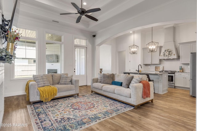 living area with visible vents, light wood-style flooring, a tray ceiling, arched walkways, and crown molding