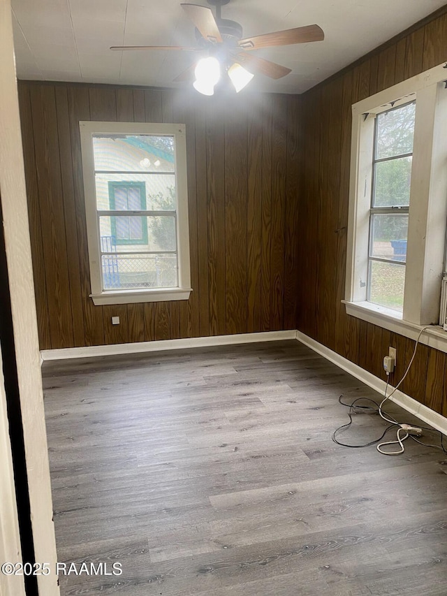 unfurnished room with wood walls, wood finished floors, a ceiling fan, and baseboards