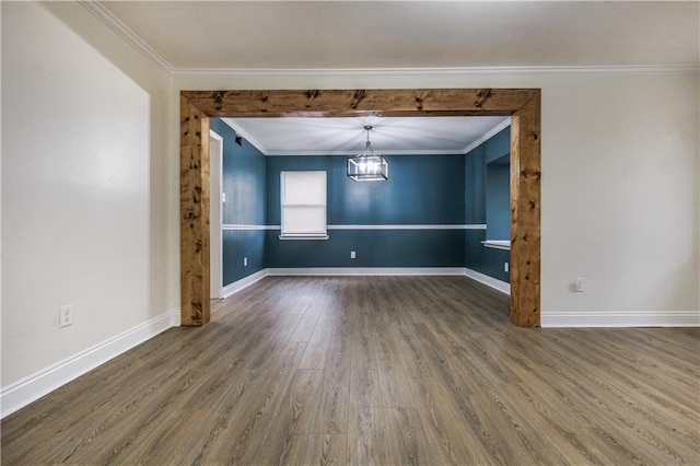 empty room featuring a chandelier, ornamental molding, baseboards, and wood finished floors