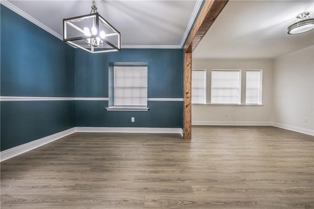 unfurnished room featuring a notable chandelier, baseboards, crown molding, and wood finished floors