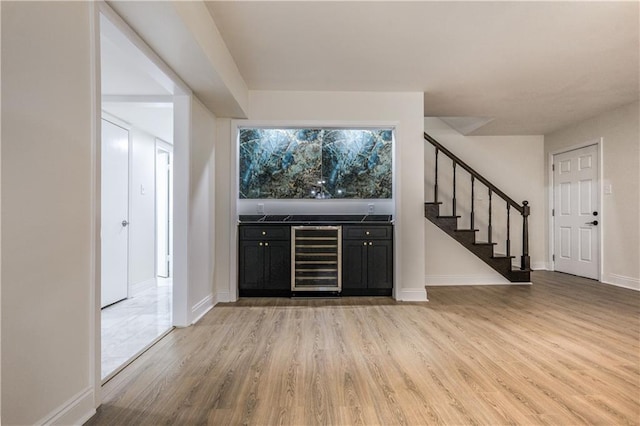 bar with light wood-style floors, beverage cooler, stairs, and baseboards