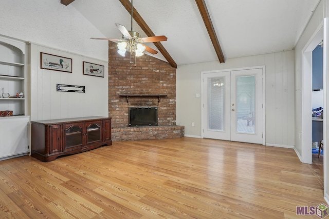 unfurnished living room with built in features, lofted ceiling with beams, light wood-style flooring, french doors, and a fireplace