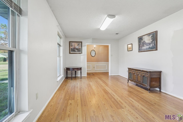 interior space with light wood finished floors, baseboards, visible vents, and a textured ceiling