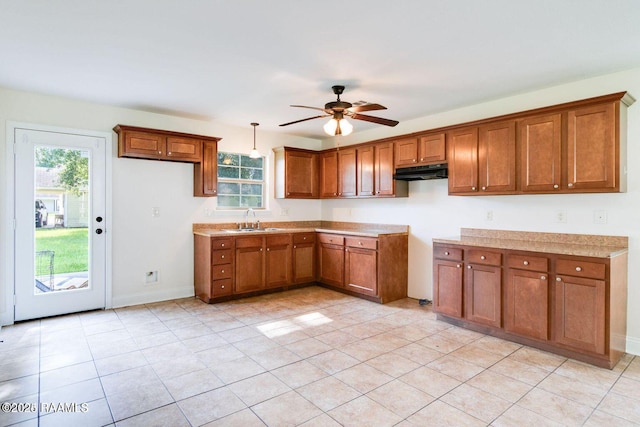 kitchen featuring under cabinet range hood, a sink, light countertops, brown cabinets, and pendant lighting