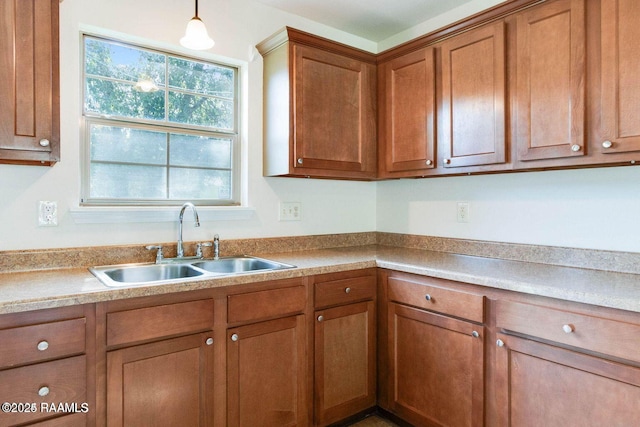 kitchen with brown cabinets, pendant lighting, light countertops, and a sink