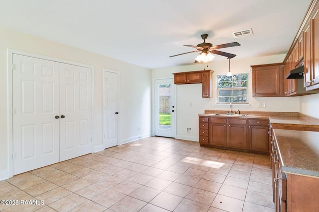 kitchen with under cabinet range hood, a sink, visible vents, light countertops, and brown cabinetry