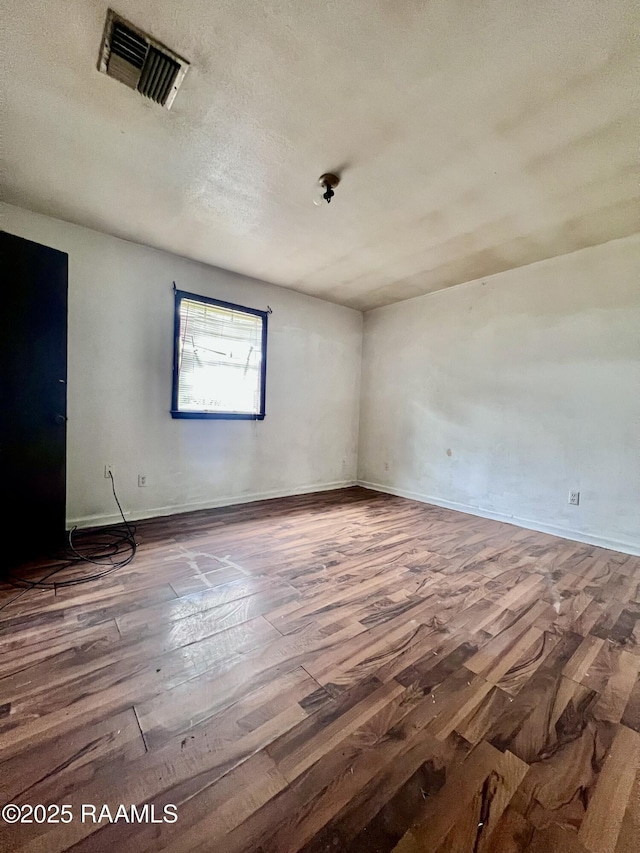 unfurnished room featuring visible vents, a textured ceiling, baseboards, and wood finished floors