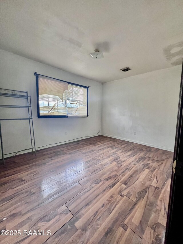 empty room with wood finished floors, visible vents, and baseboards