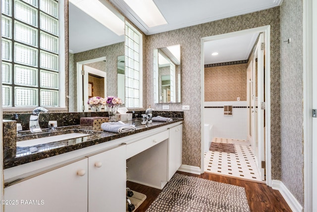 bathroom featuring double vanity, wood finished floors, a sink, ornamental molding, and wallpapered walls