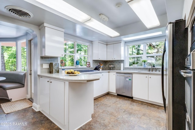 kitchen with a sink, stainless steel appliances, a peninsula, decorative backsplash, and visible vents