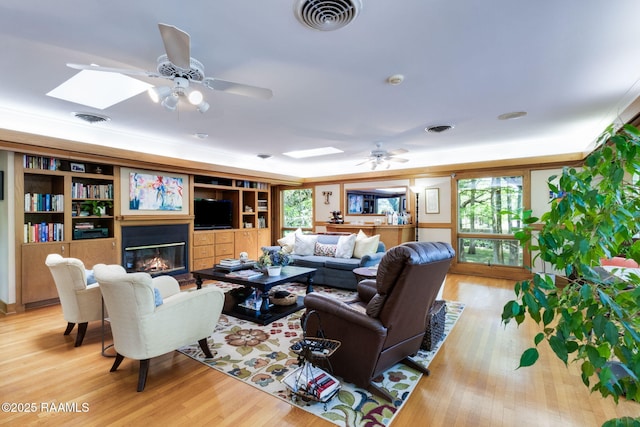 living room with a glass covered fireplace, ceiling fan, ornamental molding, and visible vents