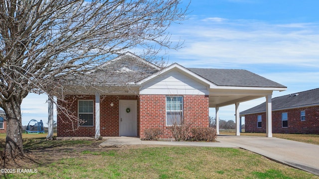 view of front of property featuring a trampoline, brick siding, concrete driveway, an attached carport, and a front lawn