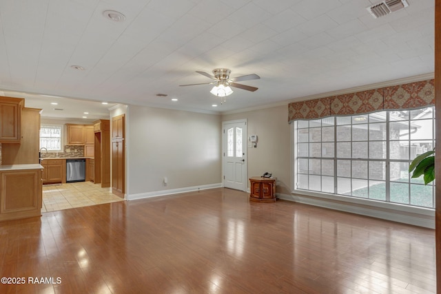 unfurnished living room with light wood-style flooring, a ceiling fan, visible vents, baseboards, and ornamental molding