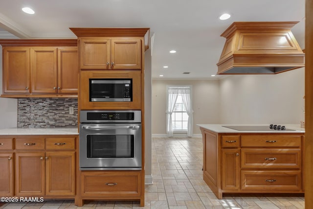 kitchen featuring stainless steel appliances, premium range hood, light countertops, ornamental molding, and decorative backsplash