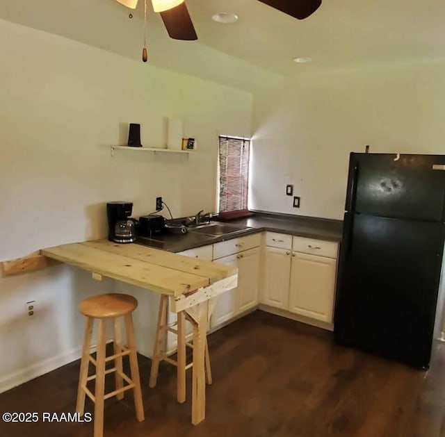 kitchen with a ceiling fan, a sink, dark countertops, freestanding refrigerator, and dark wood-style flooring