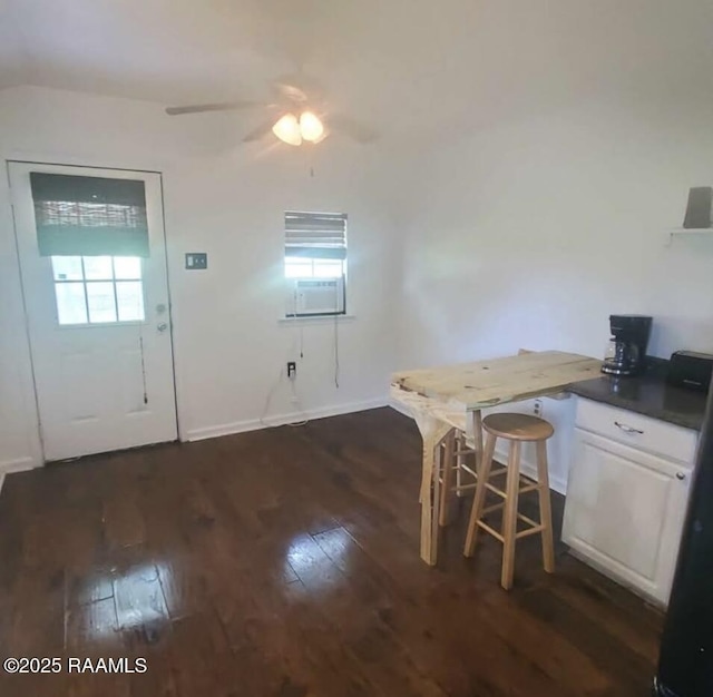 interior space featuring a ceiling fan, baseboards, dark wood-style flooring, white cabinetry, and dark countertops