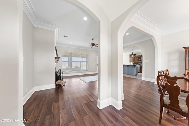 hallway with arched walkways, crown molding, baseboards, and wood finished floors