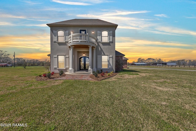 view of front of house with stucco siding, a front yard, and a balcony