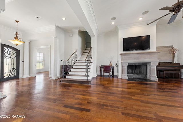 entrance foyer with wood finished floors, a ceiling fan, ornate columns, a fireplace with flush hearth, and stairs