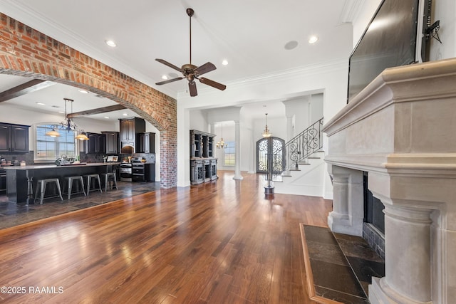 living area with arched walkways, a healthy amount of sunlight, stairs, and dark wood-type flooring