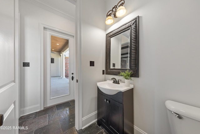 half bathroom with stone tile flooring, toilet, vanity, and baseboards