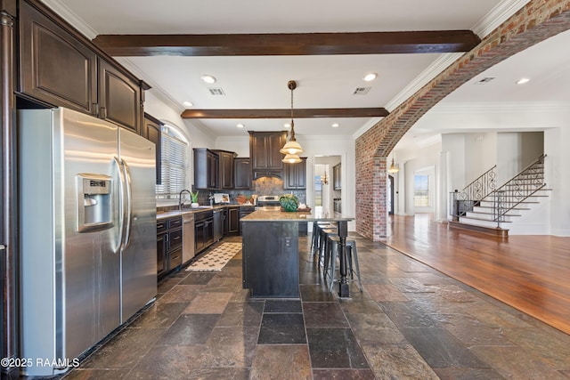 kitchen featuring dark brown cabinets, a center island, beam ceiling, stone tile flooring, and stainless steel appliances