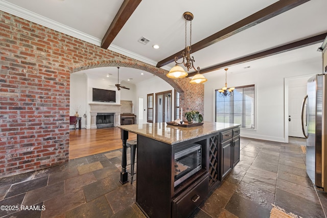 kitchen with beamed ceiling, stone tile floors, arched walkways, appliances with stainless steel finishes, and baseboards