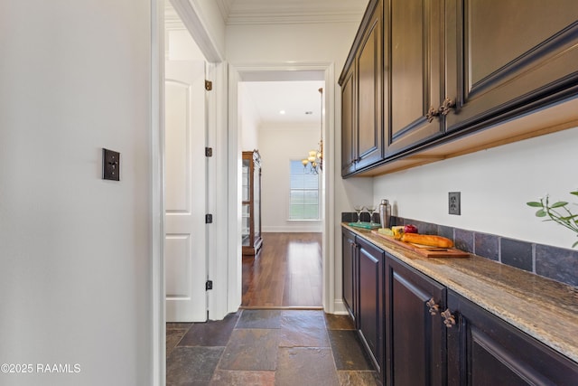 bar with stone tile floors, an inviting chandelier, crown molding, and baseboards