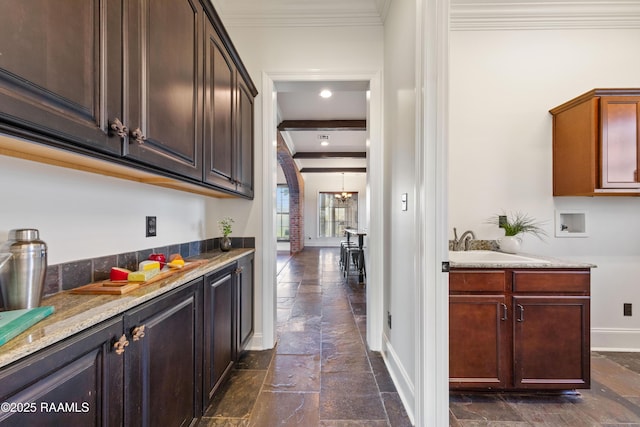 bar featuring a sink, baseboards, stone tile floors, and ornamental molding