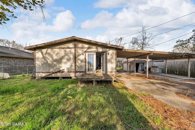 back of property with a carport, fence, driveway, and a lawn