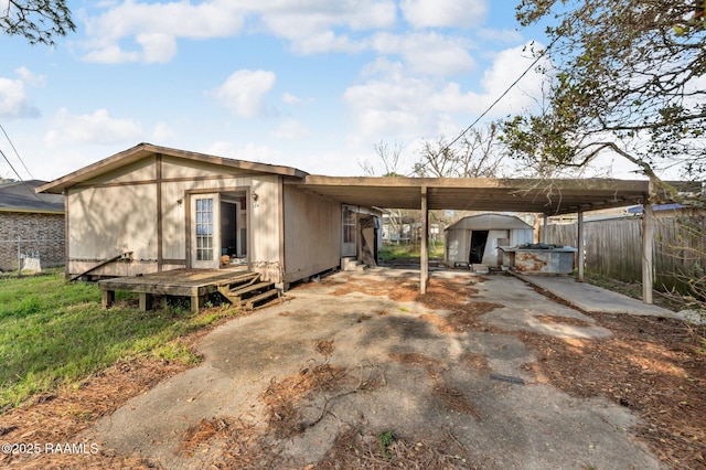 rear view of house with an attached carport, fence, driveway, and an outdoor structure