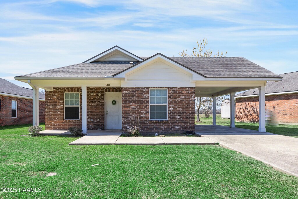 1211 Lombard St, New Iberia, LA 70560 - view of front of house featuring roof with shingles, a front lawn, concrete driveway, and brick siding