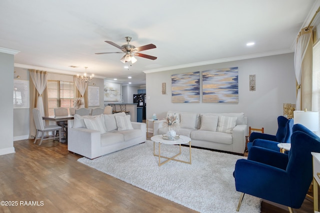 living room with ceiling fan with notable chandelier, ornamental molding, wood finished floors, and baseboards