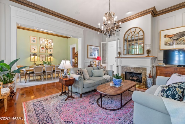 living area with a decorative wall, a premium fireplace, wood finished floors, ornamental molding, and an inviting chandelier