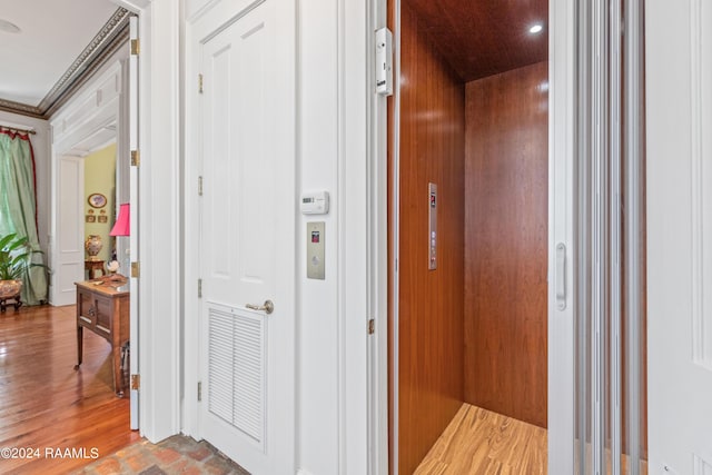 hallway with ornamental molding, wood finished floors, and elevator