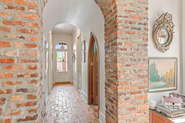 foyer with arched walkways, brick floor, and crown molding