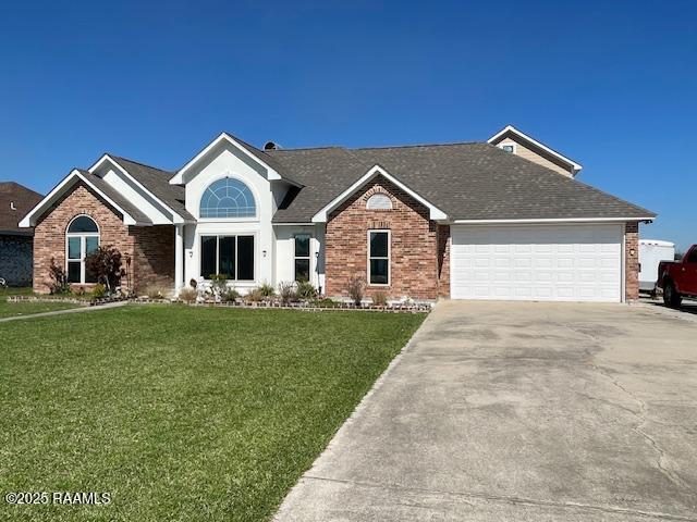 ranch-style house featuring an attached garage, a front lawn, concrete driveway, and brick siding