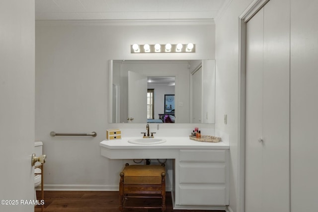 bathroom featuring baseboards, ornamental molding, a sink, and wood finished floors