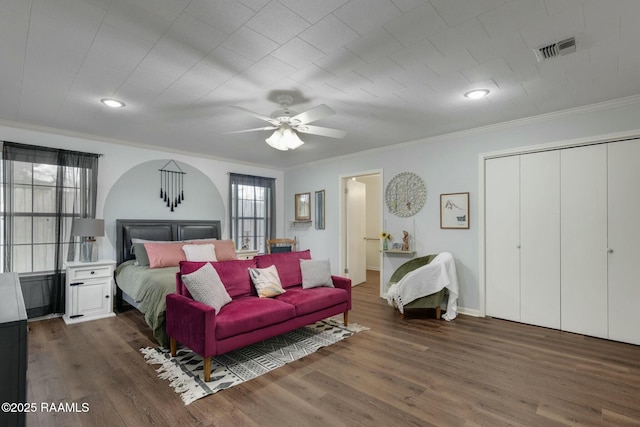 bedroom with arched walkways, crown molding, visible vents, wood finished floors, and baseboards