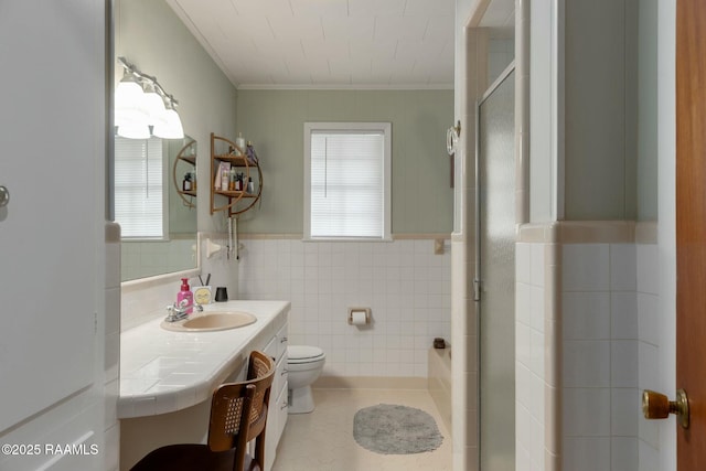 bathroom featuring toilet, a wainscoted wall, a shower with shower door, vanity, and tile walls