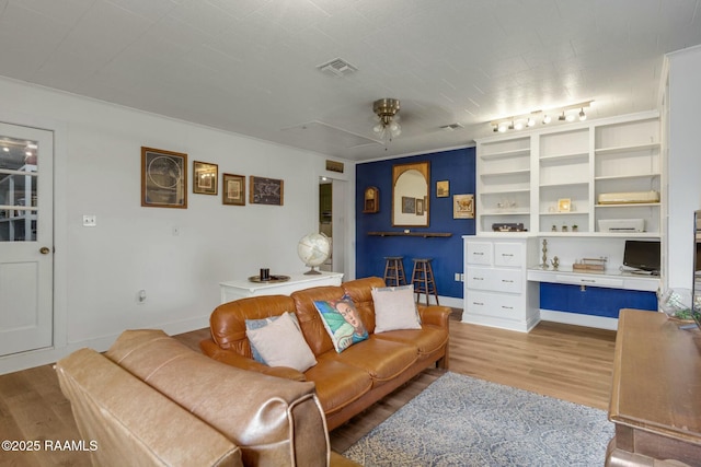 living area with baseboards, visible vents, ceiling fan, wood finished floors, and built in desk