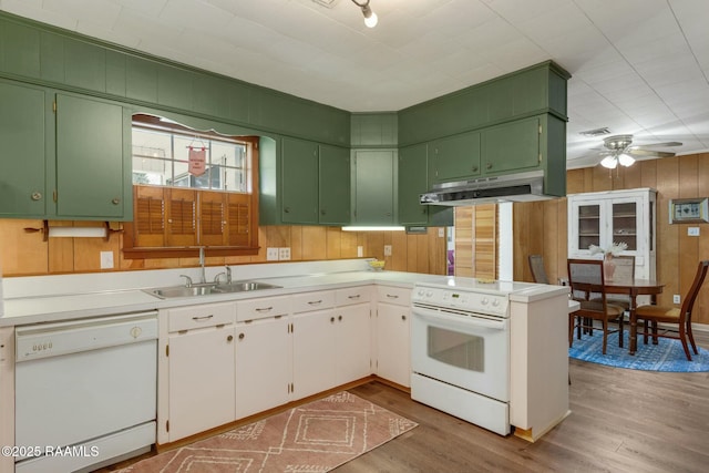 kitchen featuring white appliances, wood finished floors, wood walls, under cabinet range hood, and a sink