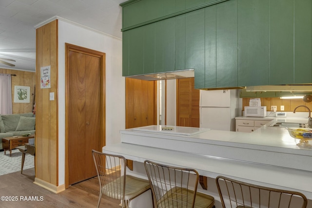 kitchen with white appliances, wood finished floors, a peninsula, crown molding, and a sink